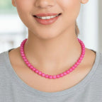Woman wearing a pink beaded necklace against a blurred indoor background