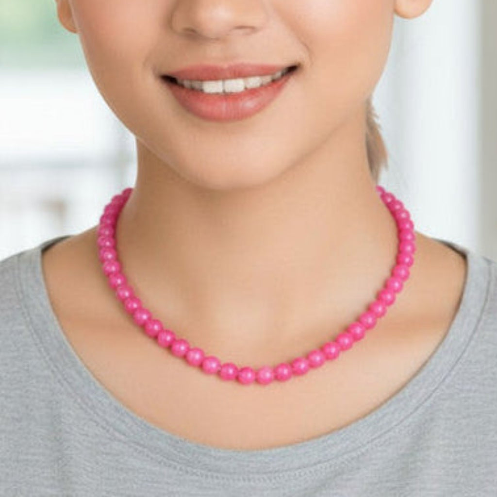 Woman wearing a pink beaded necklace against a blurred indoor background
