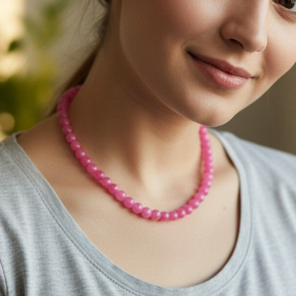 Woman wearing a pink beaded necklace indoors with a blurred background