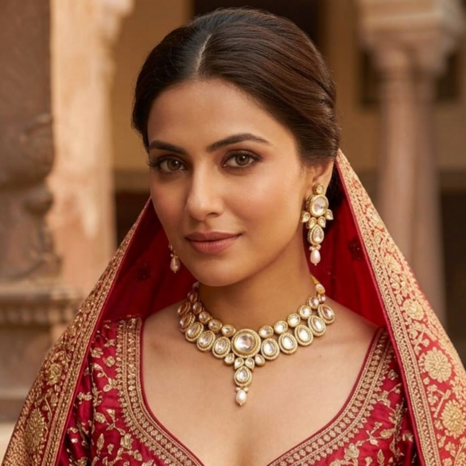 JewelOn Kundan choker necklace and earrings set with pearls and clear stones on a woman in a red embroidered outfit.